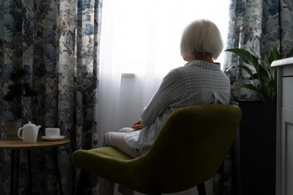 Mujer de la tercera edad sentada mirando una ventana con cortinas cerradas